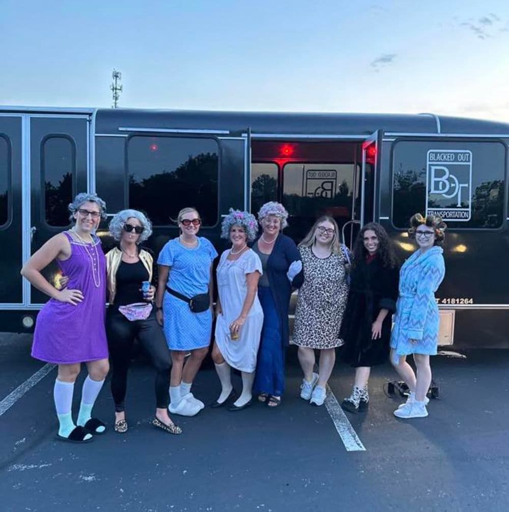 Group of women in costumes posing by a party bus, showcasing fun and lively atmosphere.