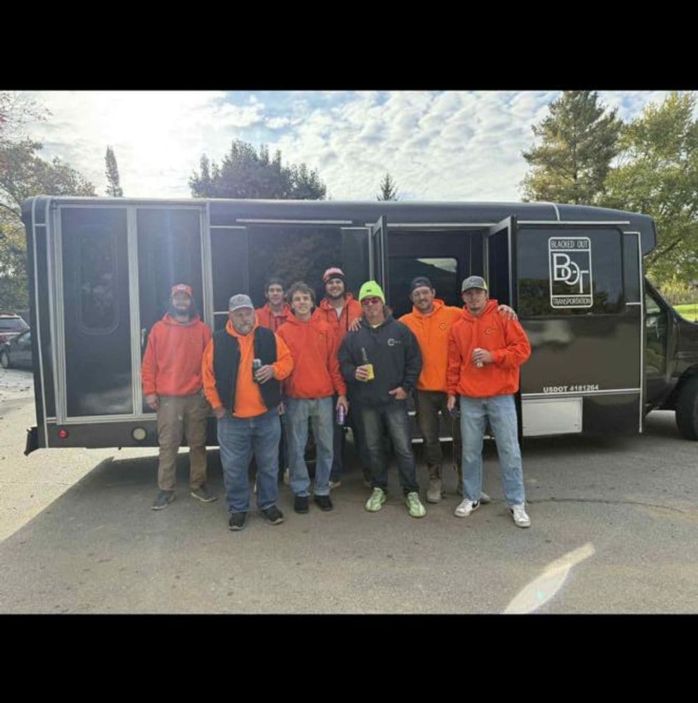 Group of workers in orange jackets posing by a black food truck on a sunny day.