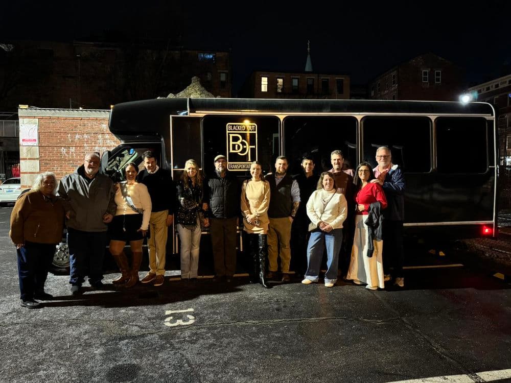Group of people posing in front of a stylish black party bus at night.