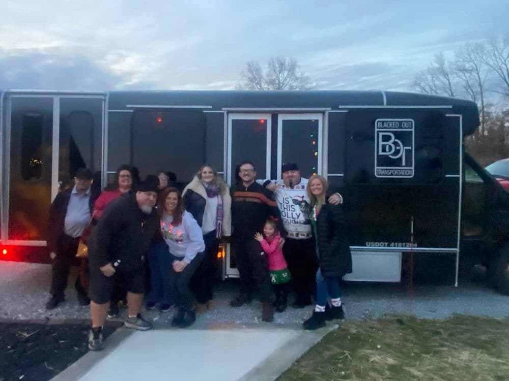 Group of friends celebrating outside a black transportation bus during twilight.