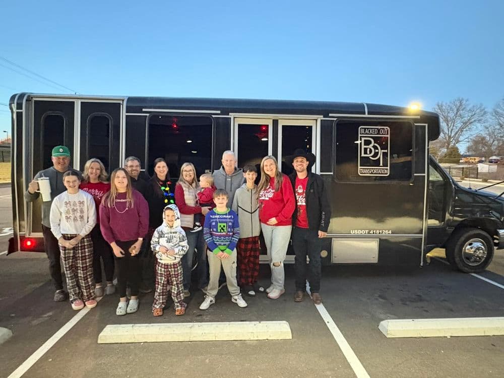 Group of people in pajamas posing in front of a black bus at sunset.