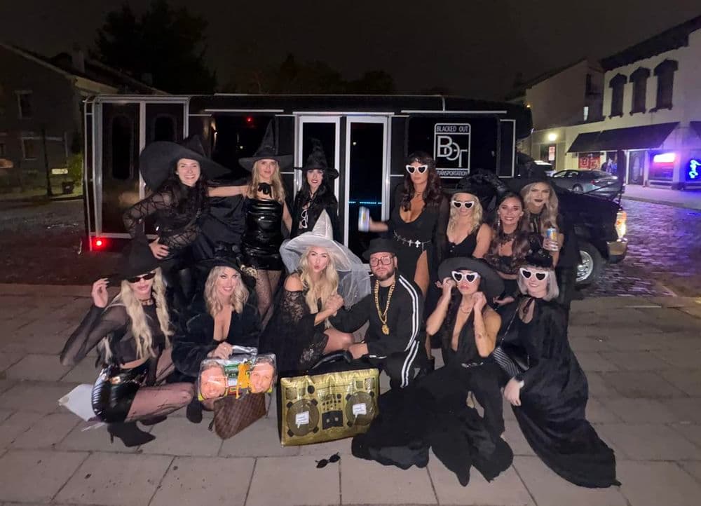 Group of women in witch costumes posing at night with a party bus in the background.
